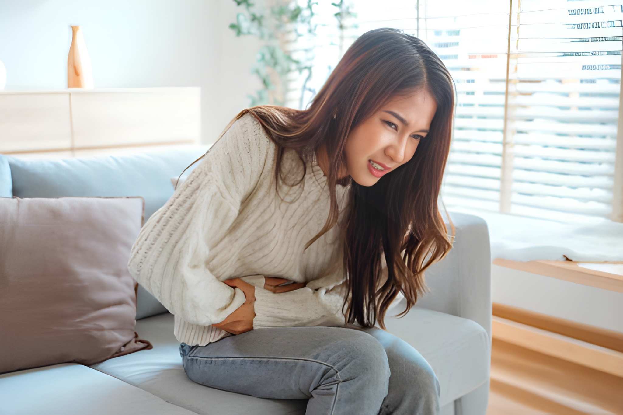 Person holding stomach in discomfort while sitting, representing symptoms addressed through ayurvedic treatment for gastritis.