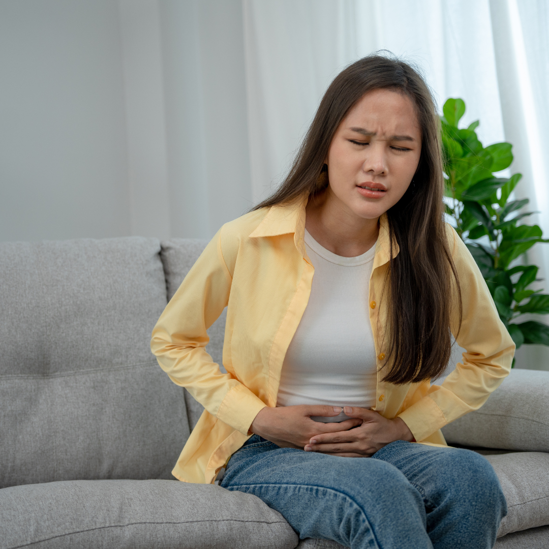 Treatment for Gastritis in Ayurveda – Natural Healing for Digestive Relief Woman experiencing stomach pain while sitting on a sofa, representing treatment for gastritis in Ayurveda