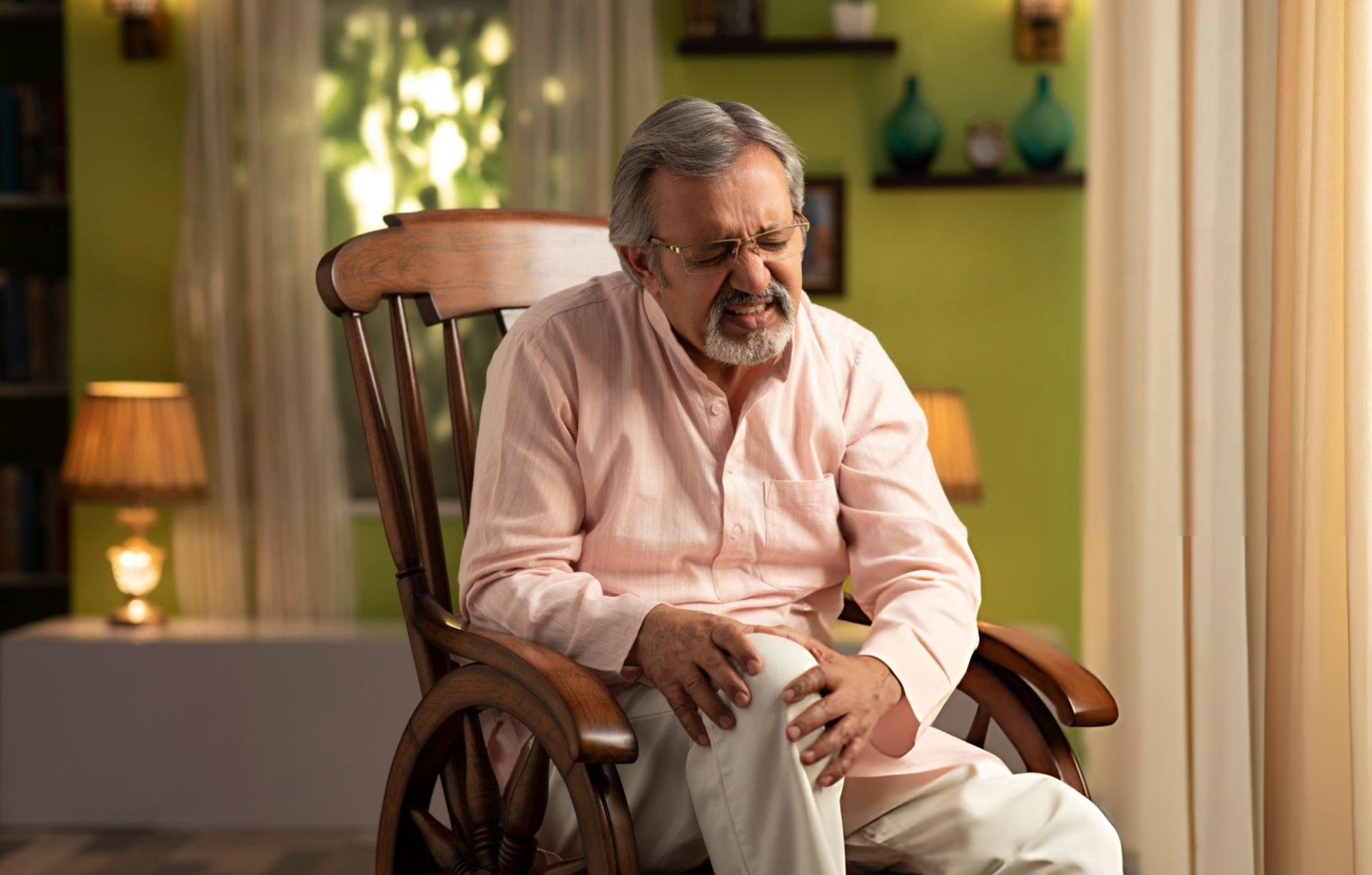 Joint Pain Ayurveda treatment for seniors, showing an elderly man holding his painful knee while seated at home, highlighting natural Ayurvedic care for joint pain relief and improved mobility.